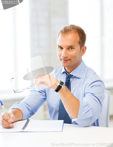 Image of businessman with spectacles writing in notebook