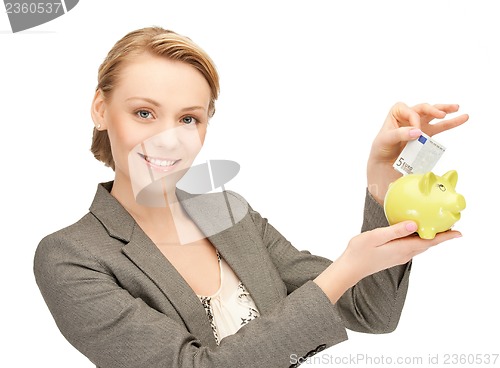 Image of woman putting cash money into small piggy bank