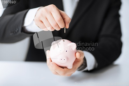 Image of man putting coin into small piggy bank