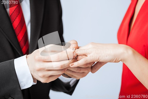Image of man putting  wedding ring on woman hand