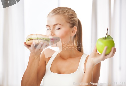 Image of woman smelling hamburger and holding apple