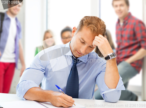 Image of handsome teacher writing in notebook