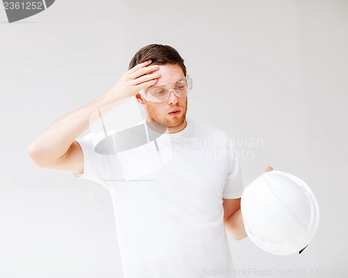 Image of male architect in safety glasses taking off helmet