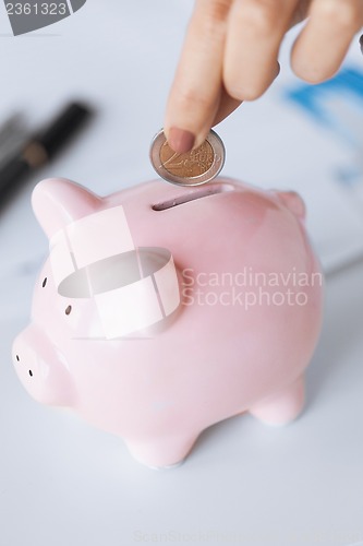 Image of woman hand putting coin into small piggy ban