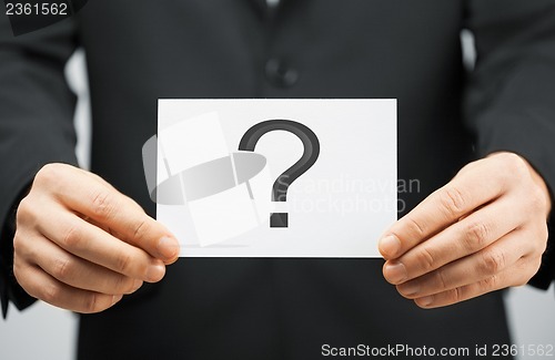 Image of man in suit holding card with question mark
