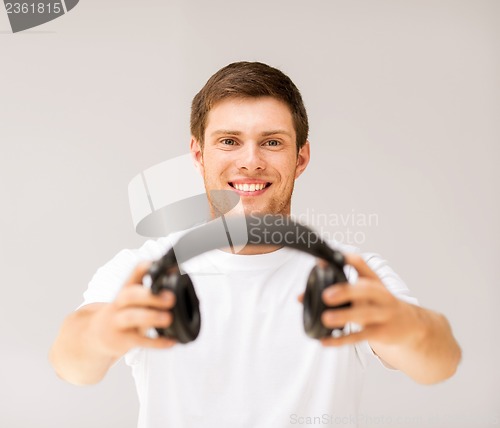 Image of young smiling man offering headphones