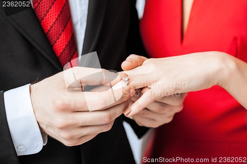 Image of man putting  wedding ring on woman hand