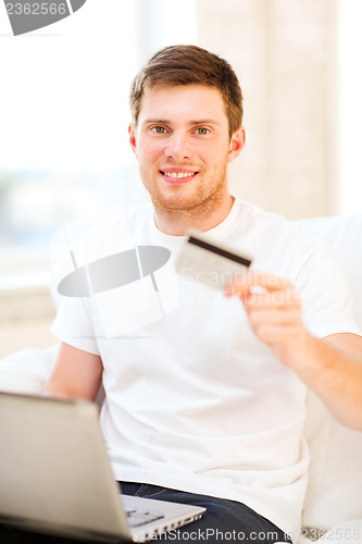 Image of man with laptop showing credit card at home