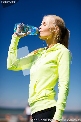 Image of woman drinking water after doing sports outdoors