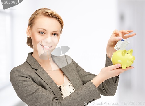 Image of woman putting cash money into small piggy bank