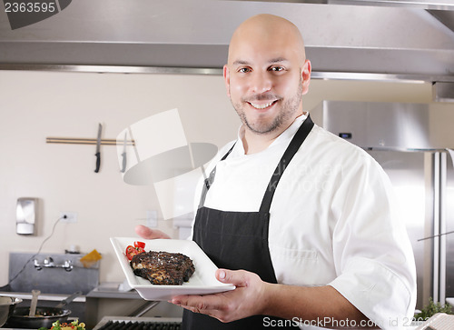 Image of young male chef presenting a juicy ribeye steak with tomatoes