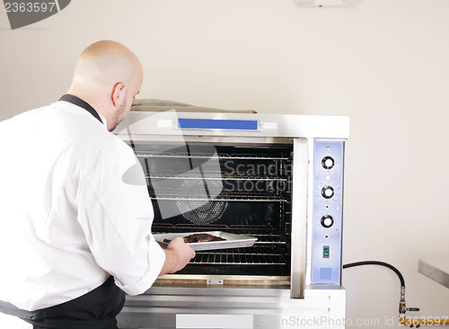 Image of chef putting a tray of a juicy steak in a professional oven