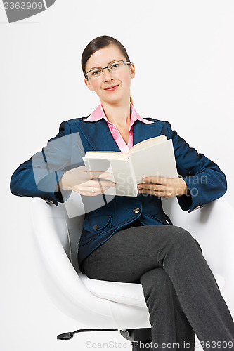 Image of A young girl sits in a white chair with a book