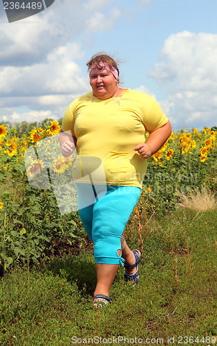 Image of overweight woman running along field of sunflowers