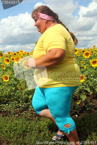 Image of overweight woman running along field of sunflowers