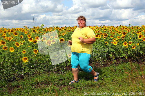 Image of overweight woman running along field of sunflowers