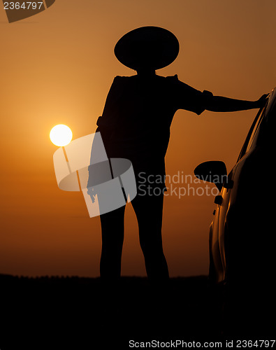 Image of Silhouette woman with hat standing near car