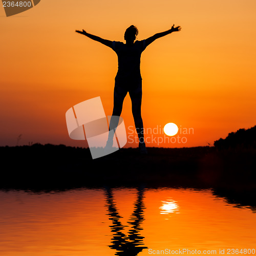 Image of Silhouette woman jumping against orange sunset