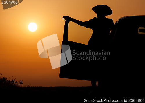 Image of Silhouette woman with hat standing near car