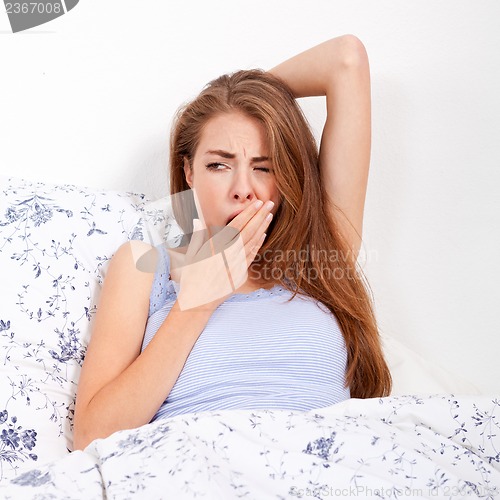 Image of young attractive woman lying in bed yawing portrait tired