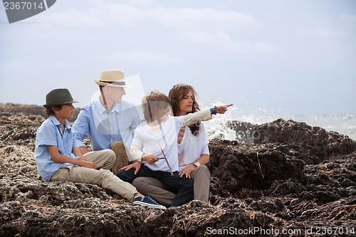 Image of happy family sitting on rock and watching the ocean waves