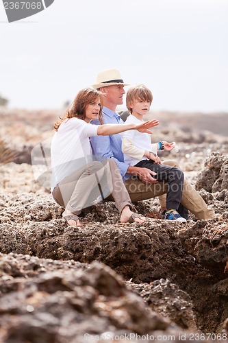 Image of happy family sitting on rock and watching the ocean waves