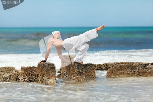 Image of healthy man doing pilates yoga meditation on beach summer