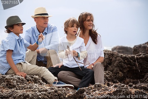 Image of happy family sitting on rock and watching the ocean waves