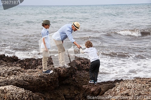 Image of happy family sitting on rock and watching the ocean waves