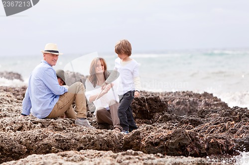 Image of happy family sitting on rock and watching the ocean waves
