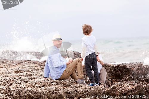 Image of happy family sitting on rock and watching the ocean waves