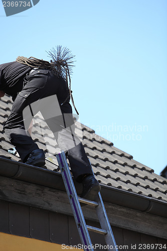 Image of Chimney sweep climbing onto the roof of a house