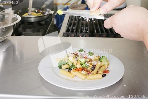 Image of Italian food. Chef putting parmesan over a rigatoni with vegetab
