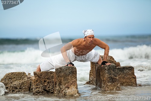 Image of healthy man doing pilates yoga meditation on beach summer