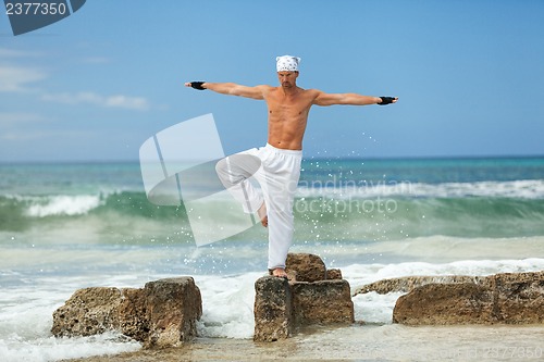 Image of healthy man doing pilates yoga meditation on beach summer