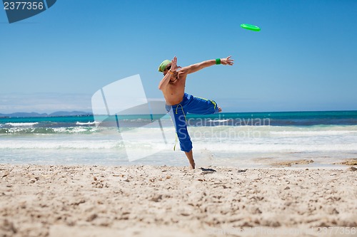 Image of attractive man playing frisby on beach in summer