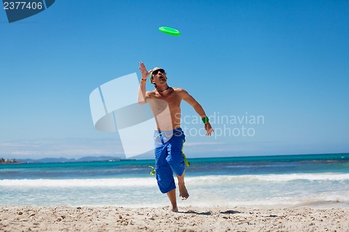 Image of attractive man playing frisby on beach in summer