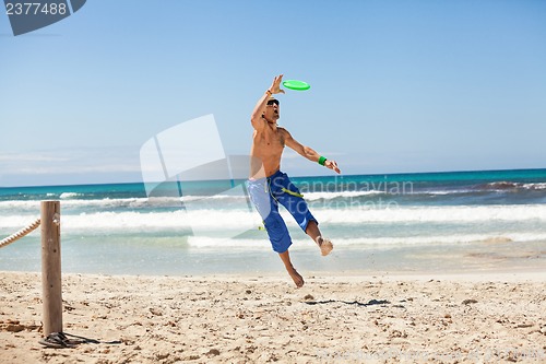 Image of attractive man playing frisby on beach in summer