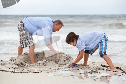 Image of father and sons on the beach playing in the sand