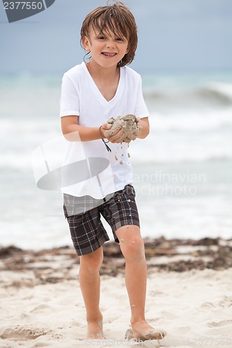 Image of cute little boy playing in sand on beach in summer