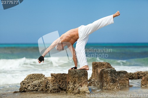 Image of healthy man doing pilates yoga meditation on beach summer