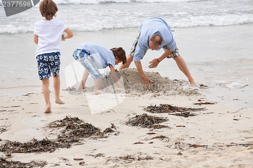 Image of father and sons on the beach playing in the sand