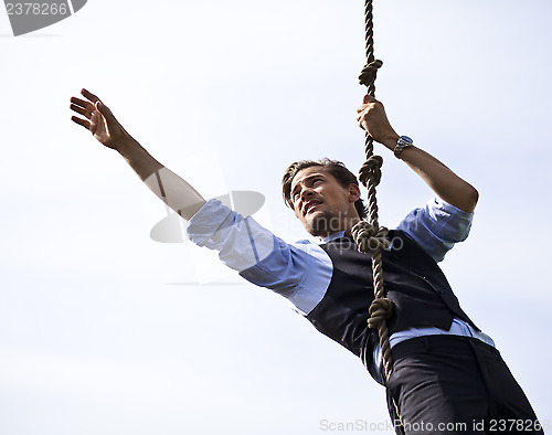 Image of Determined businessman climbing a rope, reaching