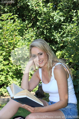 Image of Pretty smiling woman reading in the garden