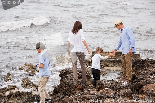 Image of happy family sitting on rock and watching the ocean waves