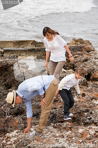 Image of happy family sitting on rock and watching the ocean waves