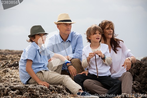 Image of happy family sitting on rock and watching the ocean waves