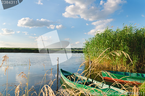 Image of beautiful river and old boats near green grass under cloudy sky