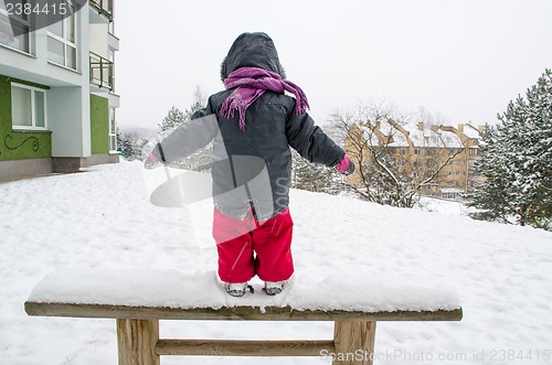 Image of child with red pants standing wooden bench snow  