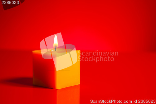 Image of Burning yellow candle over red background